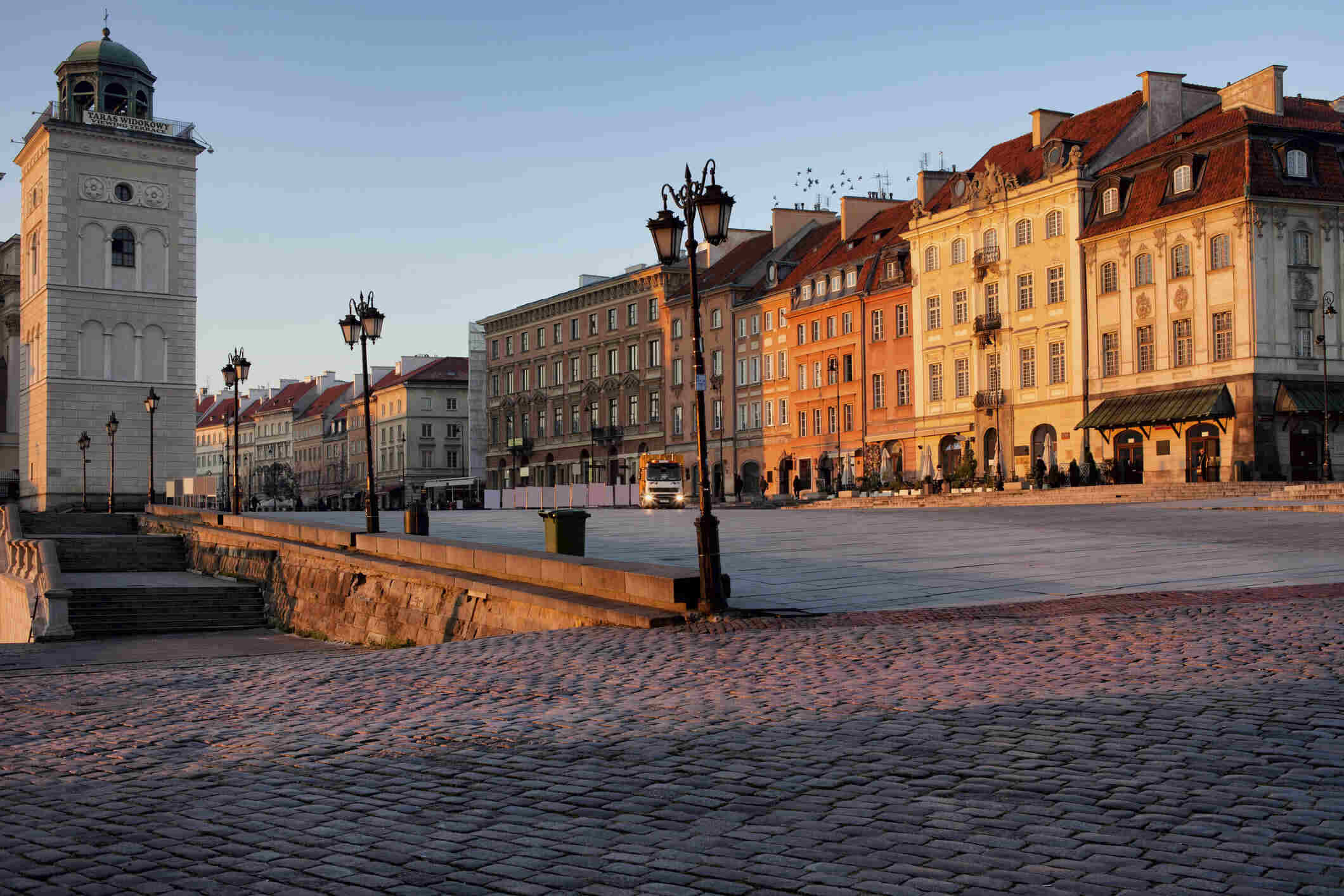 Golden morning light hitting the classic facades and cobblestone square of Warsaw, used in guides explaining Polish rental property income tax.