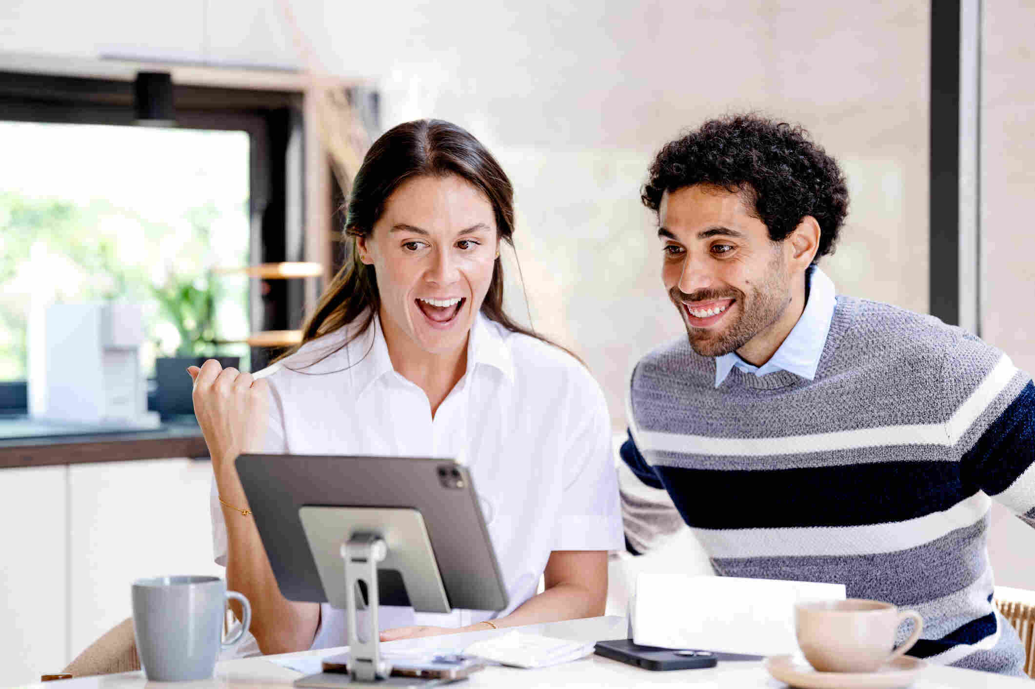 Happy couple checking property management updates as non-resident landlords on a tablet at a kitchen table